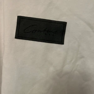 Vit t-shirt från Icono - Säljer en vit t-shirt från Icono i storlek L. Den är i nyskick och har en svart etikett med text på framsidan. Perfekt för en avslappnad stil!