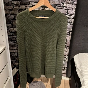 Olivgrön stickad tröja från S.C.W. - Säljer en snygg olivgrön stickad tröja från S.C.W. Den har ett fint texturerat mönster och är perfekt för kyligare dagar. Tröjan är långärmad och har ribbade muddar vid ärmslut och nederkant. Perfekt för höst och vinter! Skriv vid frågor😊