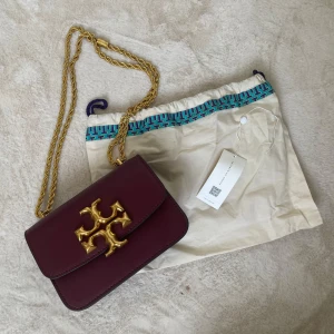 Tory Burch Eleanor Väska - Höjd: 14cm, längd: 19cm.Jättefin väska från Tory Burch vid namn Eleanor.Använd några gånger.Jag har dustbag och tagg kvar. Därav det låga utgångspriset, dustbagen är lite skrynklig men i fint skick även den.Nypris på denna modell är mellan 9-8000.