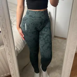 Superfina gröna högmidjade mönstrade tights från Gymshark i uppskattad storlek S, storlekslappen är avklippt, mått kan skickas. Bred resår i midjan och scrunch baktill. Inga defekter utöver att gymshark loggorna lossnat något, fint skick <3