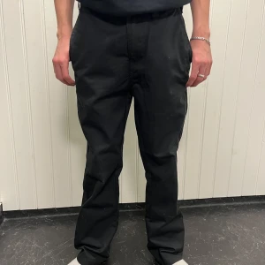 Svarta byxor från 157 - Säljer ett par stilrena svarta chinos från lager 157. De har en klassisk rak passform och är perfekta för både vardag och fest. Byxorna är i storlek S och har en enkel design utan onödiga detaljer. 