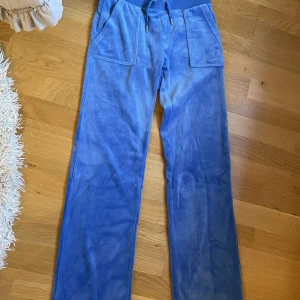 Blå mjukisbyxor från Juicy Couture - Säljer ett par superbekväma blå mjukisbyxor från Juicy Couture. De har en loose passform och är gjorda i mjuk velour. Byxorna har fickor både fram och bak Perfekta för en chill dag hemma eller ute, dem är i nyskick och använda få gånger