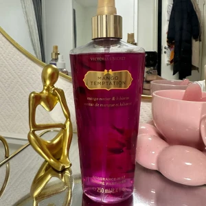 Mango Temptation Fragrance Mist från Victoria's Secret - Säljer en fräsch och exotisk doftmist från Victoria's Secret, Mango Temptation. Flaskan är genomskinlig med en härlig rosa färg och har en guldig spraypump. Doften är en blandning av mango och hibiskus, perfekt för att känna sig sommarfräsch året runt. Flaskan rymmer 250 ml och är nästan full. Perfekt för dig som älskar fruktiga och blommiga dofter!