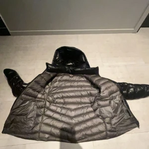 Svart dunjacka från Colmar - Säljer en snygg och varm svart dunjacka från Colmar. Jackan har en glansig finish och är perfekt för kalla dagar. Den har en dragkedja framtill och långa ärmar. Perfekt för vintern och hösten! Pris kan diskuteras han på bilden är 172