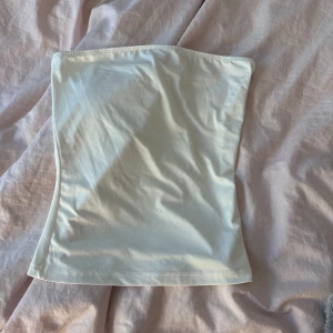 Vit tubtopp - Säljer en stilren vit tubtopp i mjukt material. Perfekt för sommardagar eller som basplagg under en kavaj. Toppen är axelbandslös och har en tight passform som sitter snyggt på kroppen.🤩