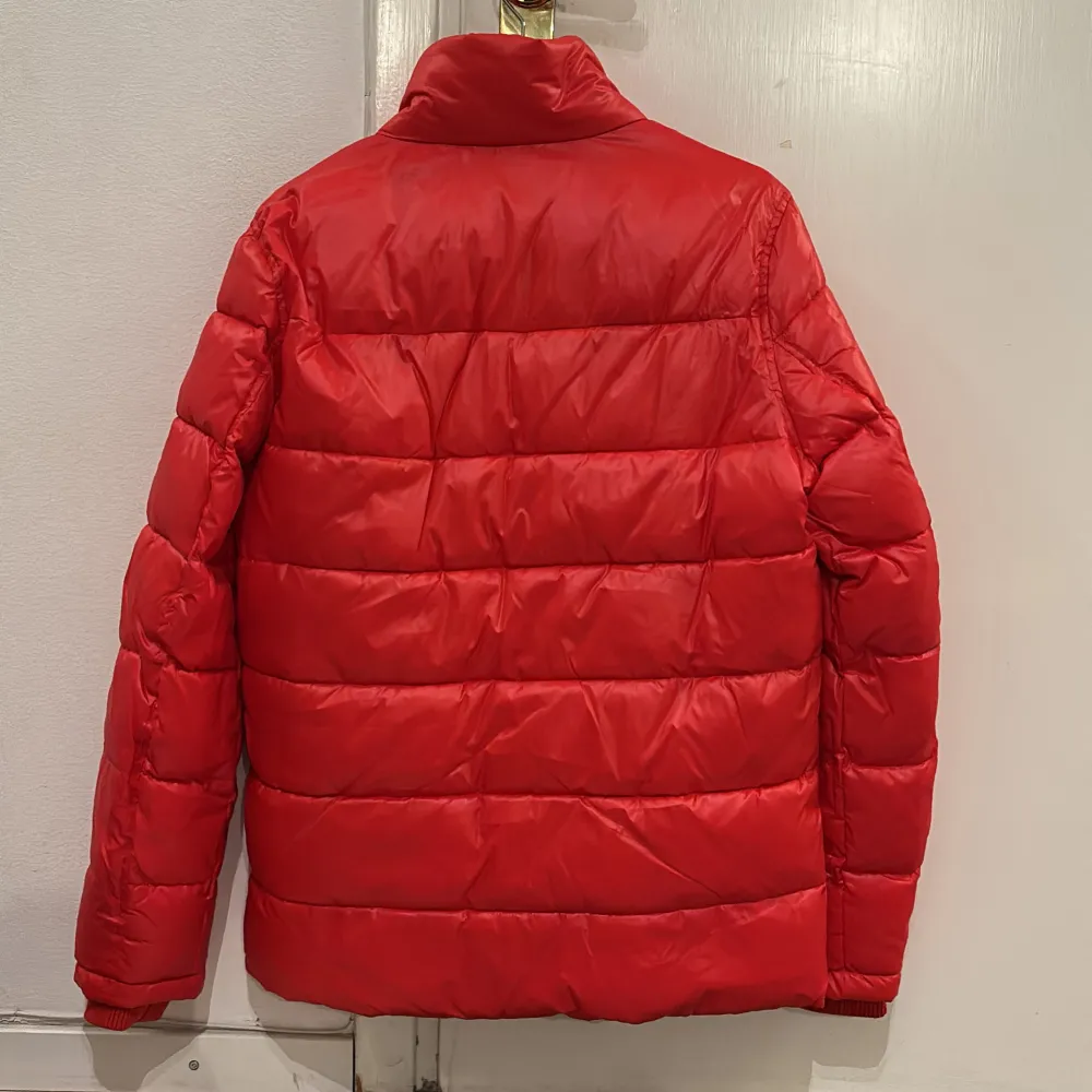 Säljer en snygg röd pufferjacka från Guess. Jackan har en hög krage och dragkedja framtill. Den är perfekt för kyligare dagar och har två praktiska fickor med dragkedjor. Guess-loggan syns tydligt på bröstet. Jackan är i bra skick och redo för nya äventyr!. Takit.