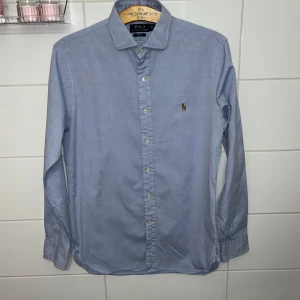Blå skjorta från Ralph Lauren - Säljer en stilren blå skjorta från Ralph Lauren i slim fit i storlek M ungefär. Skjortan har den klassiska polo Ralph lauren logo typen på bröstet. Frågor och funderingar? Hör bara av dig
