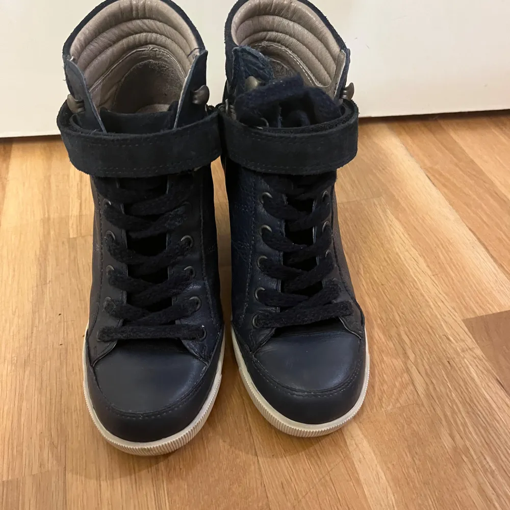 Ett par snygga Topshop mörkblå sneakers i läder med kilklack. De har en cool design med snörning och en rem med kardborreband för extra stöd. Skorna är i skinn och har en vit sula som ger en fin kontrast. Perfekta för både vardag & fest! Fint skick. Skor.