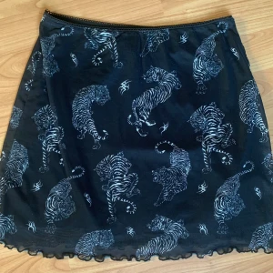 Kjol - Svart kjol med tigrar på. Svarta innerkjolen slutar strax efter rumpan. 