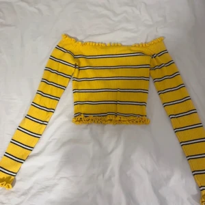 Gul randig offshoulder topp - Säljer en superfin gul offshoulder topp med svarta ränder. Den är ribbad och har långa ärmar med volangdetaljer vid kanterna. Perfekt för vår och sommar! 🖤💛 Storlek M men är liten i storleken så passar S.