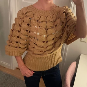 Beige stickad tröja från V London - Säljer en superfin beige stickad tröja med hål från V London. Tröjan har trekvartsärmar och en ribbad kant vid midjan som ger en snygg passform. Stilren och bekväm! 