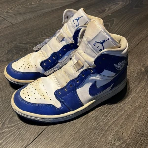 Blå Jordan 1 Mid  - Säljer mina gamla favoritskor då de inte längre kommer till användning.   De är i bra skick bortsett ifrån "skadan" på sulan (den syns och känns ej om man ej vänder på skon)   De är köpta ifrån Merch Sweden för 2300 kr, skosnören tillkommer☺️