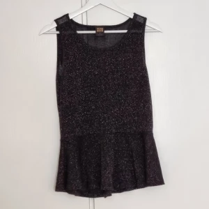 Vero Moda svart glittrig peplum topp - Snygg svart topp med glitter från Vero Moda. Toppen har en vidd vid nederkanten.