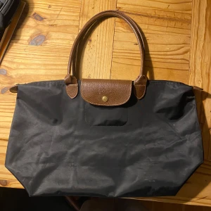 Longchamp väska - En svart handväska med läder detaljer. Finns några små vita fläckar på den kan gå bort i tvätten men har inte provat. Skriv om fler bilder. 