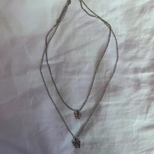 Halsband  - Fint silvrigt halsband i med två kedjor, en fjäril på varje kedja. 