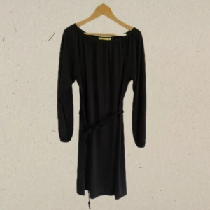 Långärmad svart klänning  - Båtringad svart klänning med stickad midjeskärp 