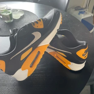 Nike Air Max  - Säljer ett par snygga Nike Air Max sneakers i svart och orange. De har en cool design med vita detaljer och en bekväm sula. Skorna är i nyskick