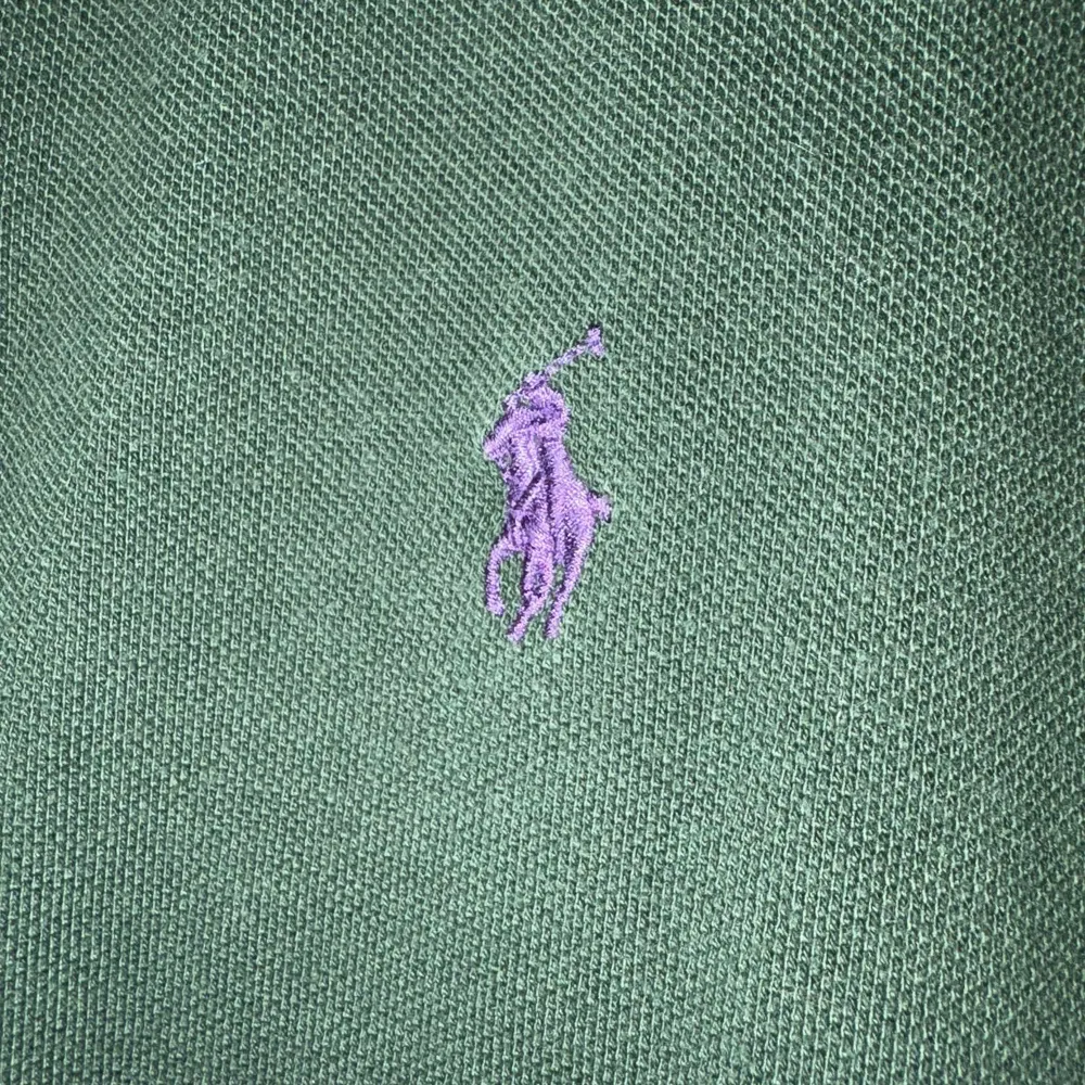 Säljer en snygg grön pikétröja från Ralph Lauren i slim fit. Den har en klassisk krage och korta ärmar, med det ikoniska lila broderade logotypen på bröstet. Perfekt för både vardag och lite finare tillfällen. Passar bra till jeans eller chinos!. Tröjor & Koftor.