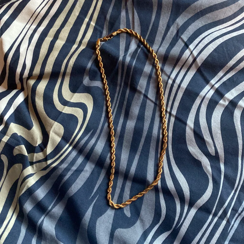 Säljer ett snyggt guldfärgat halsband med en tvinnad design. Perfekt för att ge lite extra stil till din outfit. Halsbandet har en enkel låsmekanism som gör det lätt att ta på och av. Passar både till vardags och festliga tillfällen. Ett måste för dig som gillar att sticka ut! OBS DET ÄR INTE GULD FET ÄR ROSTFRITTSTÅL. Asusteet.