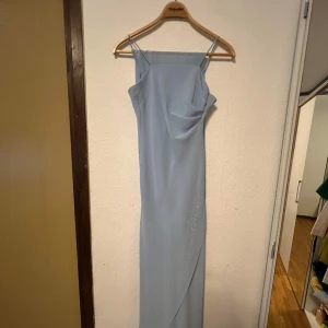 Ljusblå långklänning från Juliet - Säljer en elegant ljusblå långklänning från Juliet i storlek small med sjal. Klänningen är tillverkad i 100% polyester och har en stilren design med smala axelband. Perfekt för sommarens fester eller en fin middag. Den är i mycket bra skick och redo att bäras av någon som vill känna sig extra speciell. 