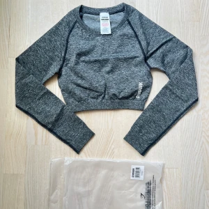 Grå croppad tröja från Gymshark - Säljer en snygg grå croppad tröja från Gymshark i nytt skick. Perfekt för träning eller en avslappnad dag. Tröjan är långärmad och har en tight passform som framhäver figuren. Materialet är mjukt och stretchigt för bästa komfort. Passa på att köpa denna stilrena tröja! 🖤