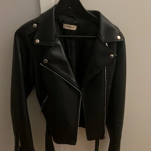 Svart skinnjacka från Glamorous - Säljer en snygg svart skinnjacka från Glamorous i storlek M. Jackan har en cool bikerstil med dragkedja och knappar. Perfekt för höst och vår, och funkar lika bra till fest som till vardags. Den är i mycket bra skick och har en klassisk look som aldrig går ur tiden.