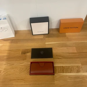 Brun plånbok i skinn - Säljer en elegant brun plånbok i mörker maral leather den är i skinn med flera fack för kort och en transparent ficka för ID. Den kommer i en stilren svart låda med röd insida. Perfekt för att hålla ordning på dina kort och kontanter med stil.