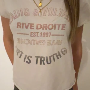 Vit t-shirt från Zadig & Voltaire - Säljer en snygg vit t-shirt från Zadig & Voltaire med tryck i rött och svart. Texten 'Rive Droite' och 'Art is Truth' ger en cool vibe. Perfekt för en casual look eller att styla upp med accessoarer. T-shirten är i bra skick och passar till allt💖