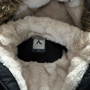 Svart vinterjacka från McKinley - Säljer en svart vinterjacka från McKinley i storlek 158. Jackan har en mysig fuskpälsfodrad huva och är perfekt för kalla vinterdagar. Den har långa ärmar och stängs med dragkedja och knappar. Perfekt för både vardag och vinteräventyr! ❄️Knappt använd, jättefint skick! Nypris ca 1000kr