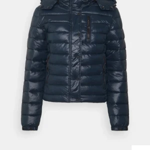 Mörkblå jacka - Säljer en snygg mörkblå dunjacka i mycket bra skick från Superdry. Jackan har en praktisk huva och dragkedja framtill. Den är långärmad och har en stilren design som passar till det mesta. Supermysig och varm!