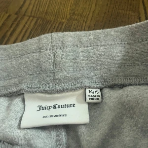 Grå mjukisbyxor från Juicy Couture - Säljer ett par grå mjukisbyxor från Juicy Couture i storlek 14/15. Byxorna har en bekväm passform med glittriga detaljer på sidan. Använda typ 3 gånger och inte alls slitna. Säljer då dem är för långa och stora i midjan. Skriv om ni undrar något och pris kan diskuteras💗