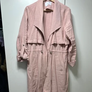 Ljusrosa trenchcoat - Säljer en superfin ljusrosa trenchcoat i bra skick. Den har långa ärmar och en snygg dragsko i midjan för en justerbar passform. Perfekt för vår och höst! 🧥