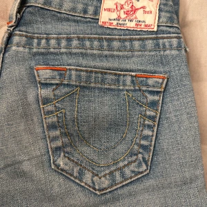Blå jeans från True Religion - Säljer ett par snygga blå jeans från True Religion. De har en låg midja och med märkets ikoniska broderi på bakfickorna. 