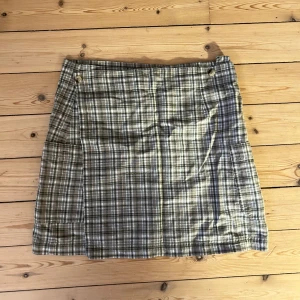 Rutig kjol i beige och grönt - Säljer en superfin rutig kjol i beige och gröna toner. Den är perfekt för både vardag och lite mer uppklädda tillfällen. Kjolen har en klassisk passform och är i ett mjukt material som känns skönt mot huden. Den är i bra skick och redo för en ny garderob!