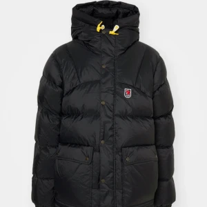 Svart dunjacka från Fjällräven - Säljer men även byter ut  en svart dunjacka från Fjällräven i mycket bra skick.  Jag kan byta ut denna jacka till en i annan färg än svart. Jackan har en praktisk huva med gula detaljer och knappar framtill. Perfekt för kalla vinterdagar med sin varma och bekväma passform. Den passar allt från storlek Xs-Xl. Den har långa ärmar och flera fickor för extra förvaring. En stilren och funktionell jacka för alla tillfällen!💕💕