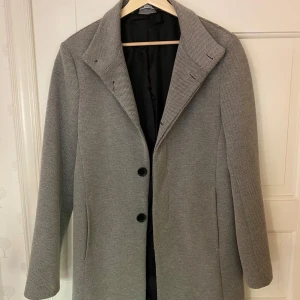 Kappa från Zara - Säljer en stilren grå kappa från Zara i storlek S. Den har en klassisk design med två knappar framtill och är perfekt för höst och vår. Kappan är i mycket bra skick och har en tidlös look som passar till alla tillfällen.