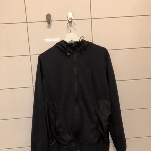 Svart hoodie från Jordan - Säljer en svart hoodie från Jordan i bra skick. Den har en dragkedja framtill och en justerbar huva. Perfekt för både träning och vardagsbruk. Den ikoniska Jumpman-loggan syns på bröstet. Skön och stilren design som passar till det mesta.