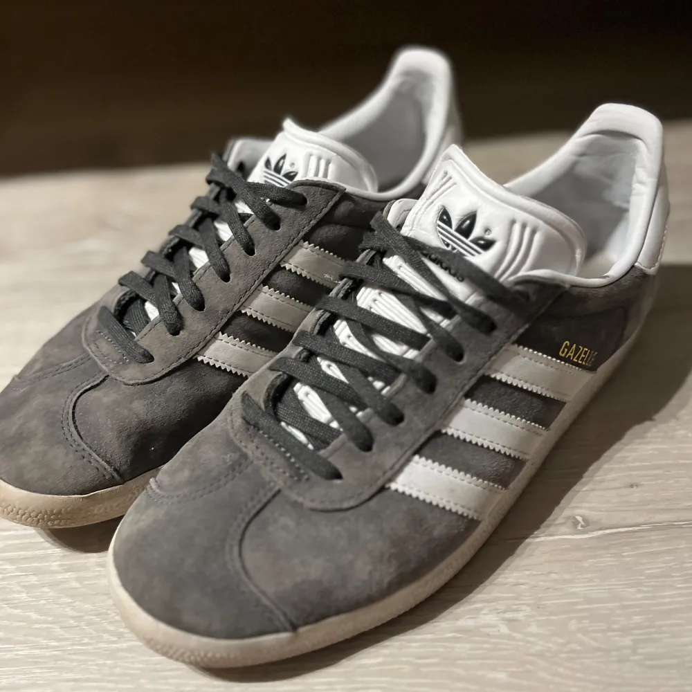 Säljer ett par snygga grå Adidas Gazelle sneakers i mocka. Storlek 41 & 1/3. De har de klassiska vita ränderna och grå / svart snörning. Perfekta för både vardag och fest! Skorna är i mycket bra skick och redo för nya äventyr.. Skor.