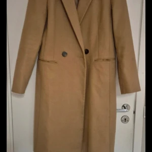 Beige kappa från Miss Selfridge - Säljer en elegant beige kappa från Miss Selfridge i storlek EUR 38. Den har en klassisk design med knappar framtill och långa ärmar. Perfekt för höst och vår, och ger en stilren look till vilken outfit som helst. Kappan är i mycket bra skick och redo för nya äventyr!