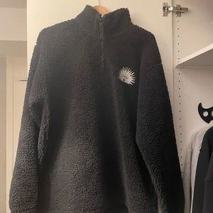 Svart fleecejacka  - Säljer en svart fleecejacka med ett coolt solmotiv och texten 'OBLIVION' på ryggen. Jackan har en dragkedja framtill och är supermjuk och varm, perfekt för kyliga dagar. Den har en avslappnad passform och är långärmad. Perfekt för höst och vinter!