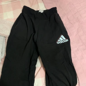 Svarta mjukisbyxor från Adidas - Säljer ett par svarta mjukisbyxor från Adidas i bra skick. De är perfekta för träning eller en chill dag hemma. Byxorna har en elastisk midja och det klassiska Adidas-loggan på benet. Superbekväma och stilrena!
