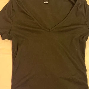 Svart ribbad topp från Shein - Säljer en svart ribbad topp från Shein i storlek M. Toppen har en v-ringad hals och korta ärmar, perfekt för både vardag och fest. Den är i bra skick och passar till många olika outfits. Säljs för 20