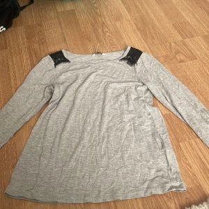 Grå långärmad tröja med spetsdetaljer - Säljer en snygg grå långärmad tröja med svarta spetsdetaljer vid axlarna. Perfekt för både vardag och lite finare tillfällen. Tröjan är i bra skick och passar åldern 11-12 år. Supermjuk och bekväm att ha på sig!