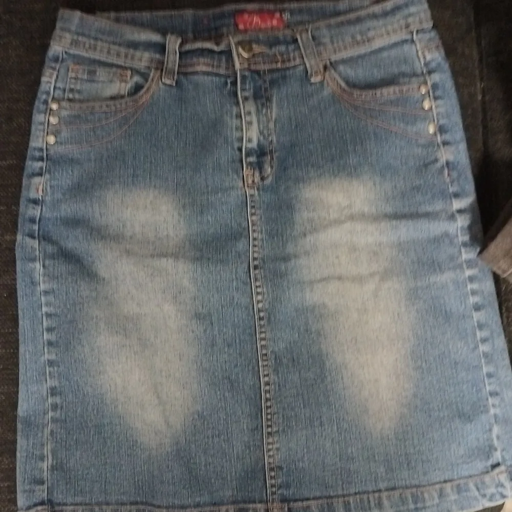 Säljer en snygg jeanskjol i klassisk blå denim med coola slitningar framtill. Kjolen har en rak passform och knappar i midjan. Perfekt för en avslappnad vardagslook eller en utekväll med vänner. Passar bra till både sneakers och klackar!. Kjolar.