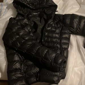 Svart pufferjacka från Boohoo - Säljer en svart pufferjacka från Boohoo i storlek S. Jackan är perfekt för kalla dagar med sin vadderade design och har en praktisk huva. Den har en dragkedja framtill och är i mycket bra skick. Perfekt för höst och vinter!