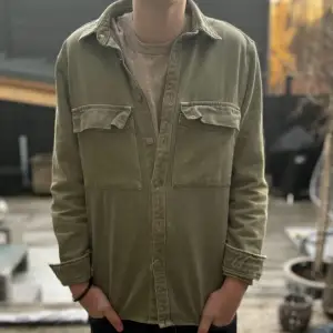 Säljer en snygg olivgrön overshirt. Perfekt för lager-på-lager-stil under hösten/vintern. Den har långa ärmar och knappar framtill samt två bröstfickor med lock. Passar både till vardags och lite mer uppklädda tillfällen. Skön och stilren! Skriv privat om ni undrar något, kan sänka priset vid snabba affärer!