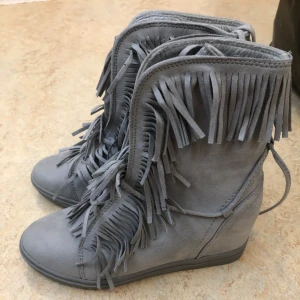 Fransskor - Säljer ett par grå boots med coola fransdetaljer. De har en bekväm kilklack och snörning framtill. Perfekta för höst och vår när du vill ha en stilren men ändå unik look. Använd dem till både vardag och fest