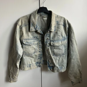 Jeansjacka från Gina Tricot - Säljer en snygg jeansjacka från Perfect Jeans i storlek M. Den har en klassisk blå tvätt och är croppad för en modern look. Jackan har långa ärmar och knappar framtill samt två bröstfickor. Perfekt för vår och sommar!