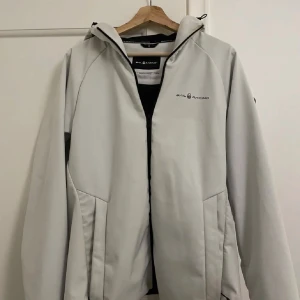 Vit jacka från Sail Racing - Säljer en snygg vit jacka från Sail Racing. Den har en dragkedja framtill och en praktisk huva. Perfekt för kyliga dagar med sin stilrena design och bekväma passform. Jackan är i mycket bra skick och passar perfekt för både vardag och utomhusaktiviteter.