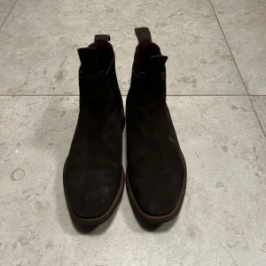 Loake bruna mocka chelsea boots - Snygga bruna chelsea boots i mocka, perfekta för höst och vinter. De har en klassisk design med elastiska paneler på sidorna för enkel på- och avtagning. Skorna är i bra skick. Nypris 4000kr